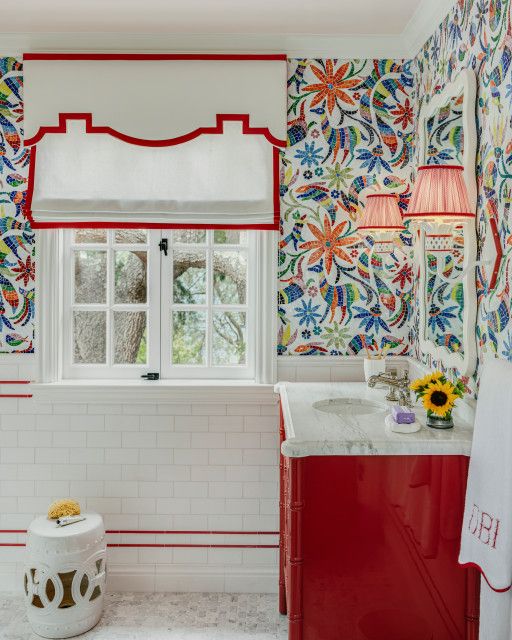 a bright bathroom with white subway tiles and marble hex ones, bold printed wallpaper, a coquelicot vanity and white and red shades