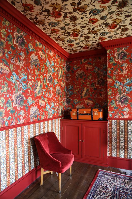 a bright coquelicot space with colorful floral wallpaper on the walls and ceiling, coquelicot cabinets, a printed rug