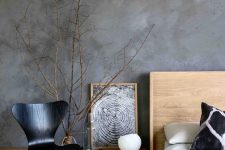 a catchy bedroom with grey limewashed walls, light-stained furniture and a black plywood chair, branches in a vase