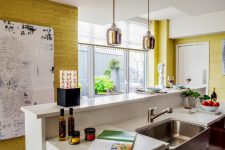 a catchy kitchen with yellow grasscloth wallpaper, a white kitchen island, pendant lamps and a bold artwork