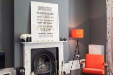 a catchy modern living room with slate grey walls, a fireplace, bold orange pieces – lamps, chairs is a chic and contrasting space