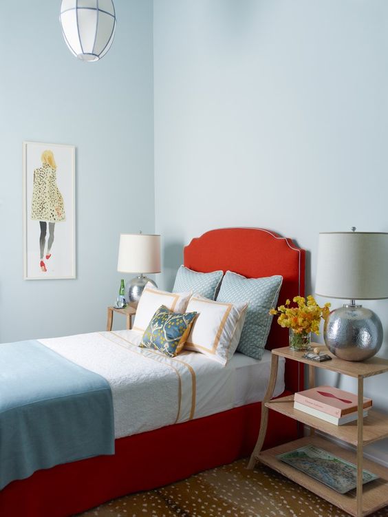 a chic guest bedroom with pastel blue walls, a coquelicot upholstered bed with blue bedding, wooden nightstands and cool table lamps