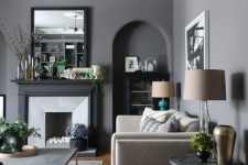 a chic living room with slate grey walls, neutral seating furniture and grey and black tables, a faux fireplace and lamps