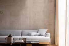 a contemporary Japandi living room with greige limewashed walls, a grey sofa and a glass coffee table plus a textural rug