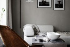 a contemporary exquisite space with light grey walls, a white sofa, a slate grey coffee table and a rug, a brown leather chair