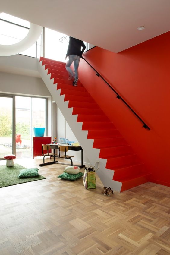 a contemporary space with a coquelicot wall and staircase, colorful pillows and rugs and bright furniture pieces