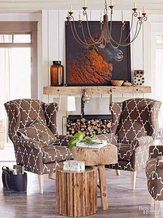 a cozy nook by the fireplace with firewood, printed chairs, a reclaimed wood mantel, a bold artwork and rough wood stools