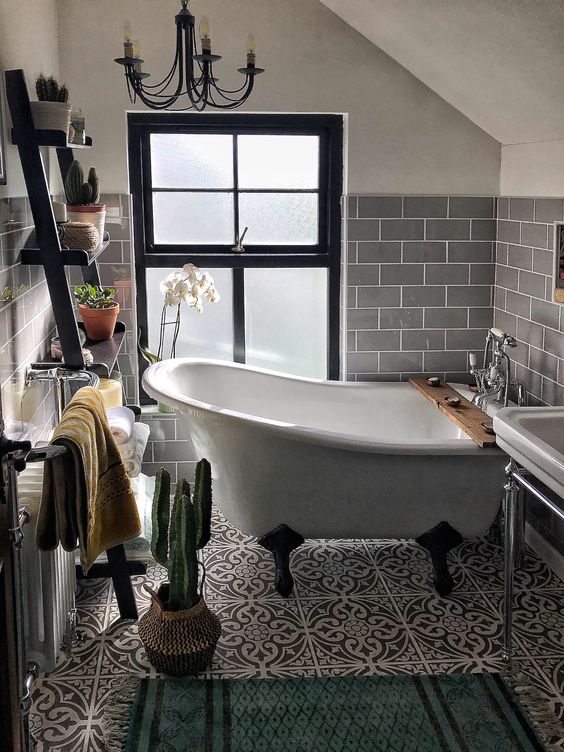 a cute small attic bathroom clad with slate grey subway tiles, with a clawfoot tub, a black ladder, a free-standing sink and a vintage chandelier