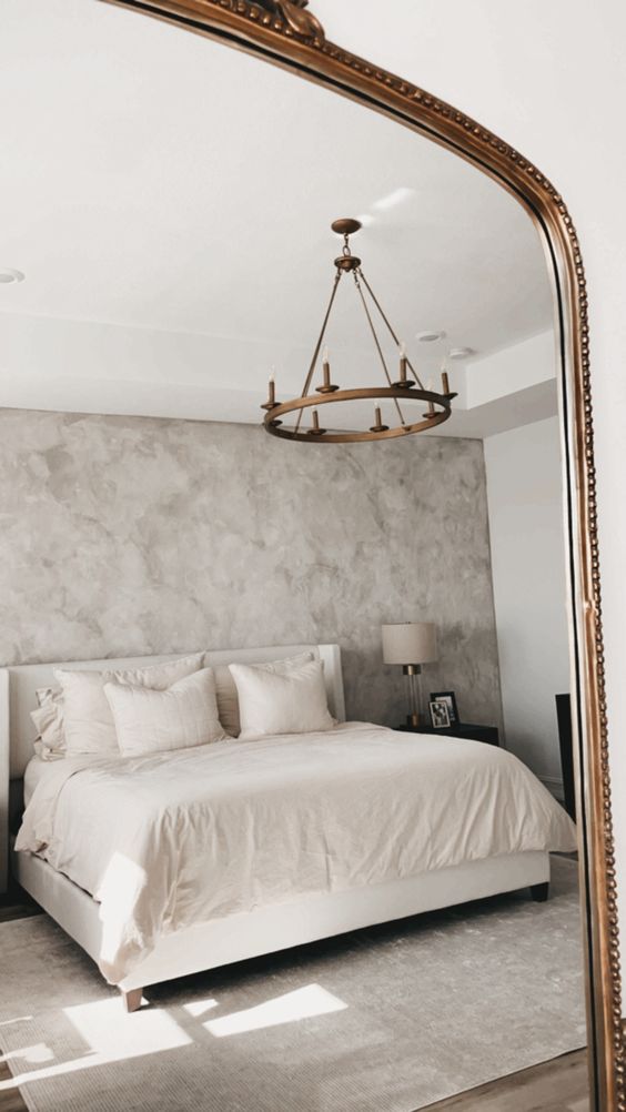 a delicate bedroom with grey limewashed walls, a creamy bed with matching bedding, black nightstands and neutral table lamps