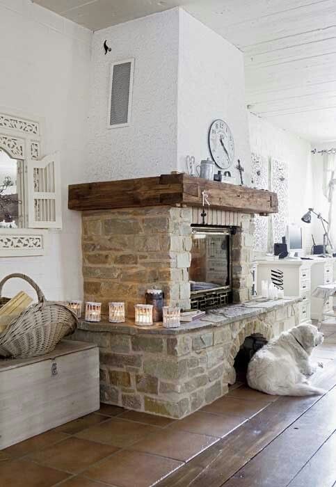 a farmhouse living room with a fireplace clad with stone and a rough wood mantel, candle lanterns and various vintage decor