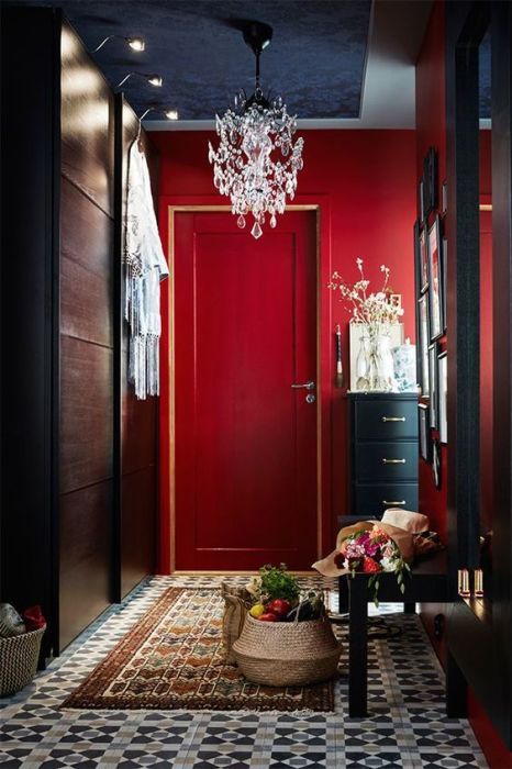 a gorgeous entryway with coquelicot walls, a dark storage unit and bench, a crystal chandelier and a small gallery wall