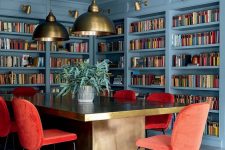 a gorgeous stone blue dining room and library in one, with a dining table with a gold tabletop and coquelicot chairs for a bold statement