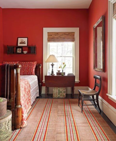 a historic bedroom with coquelicot walls, dark stained furniture, printed textiles, shades, a mirror in a frame and round boxes