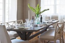 a lovely neutral dining room with farmhouse touches, with greige grasscloth wallpaper, a trestle table and neutral chairs and a tassel chandelier