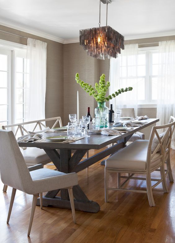 a lovely neutral dining room with farmhouse touches, with greige grasscloth wallpaper, a trestle table and neutral chairs and a tassel chandelier