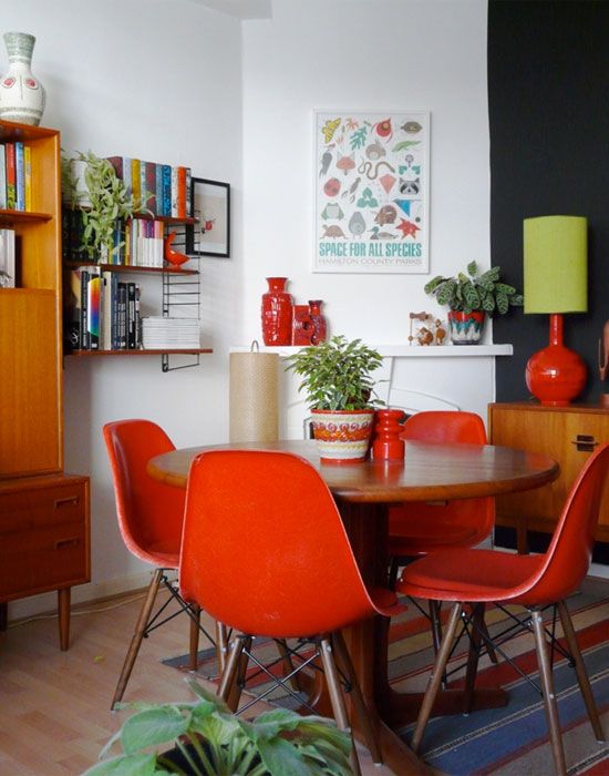 a mid century modern dining space with a stained table, coquelicot chairs, potted plants and blooms and some art