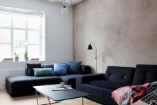 a modern living room with a greige limewashed wall, black sofas and colorful pillows, pendant bulbs and a black sconce
