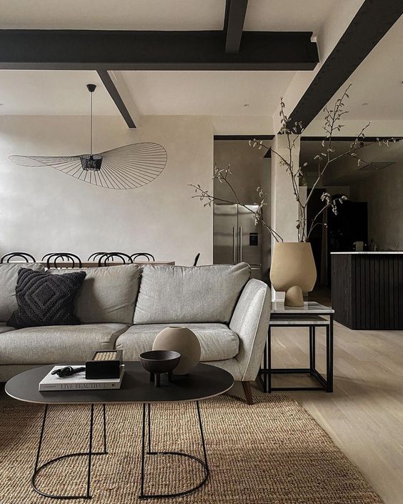 a modern space with neutral limewashed walls, a grey sofa, a black oval coffee table and a dining space