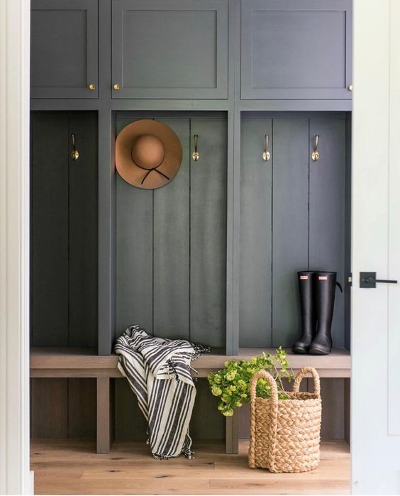a mudroom with slate grey racks and cabinets, a stained bench, a basket for storage and a striped blanket is chic