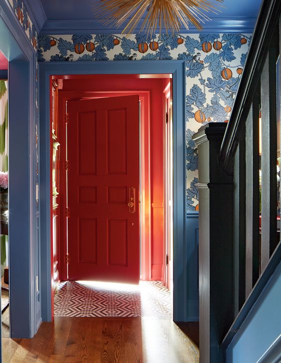 a pastel blue entryway with wainscoting and printed wallpaper, a coquelicot door and wall around it for a color statement