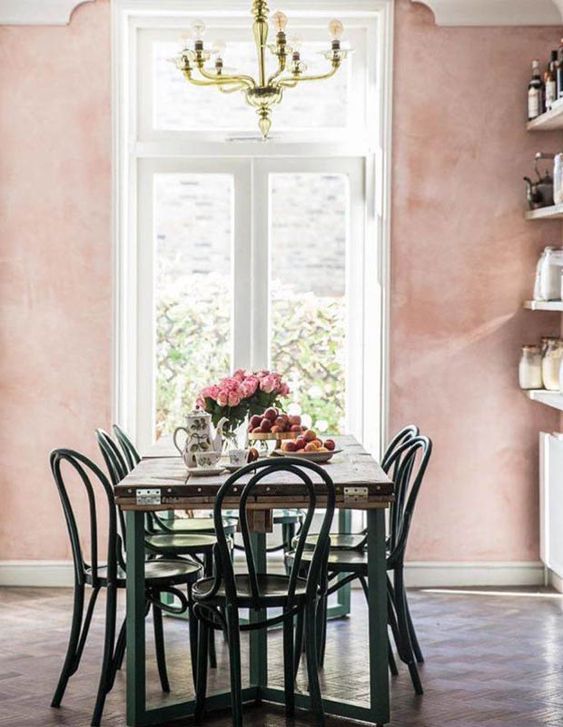 a pretty eat-in kitchen with pink limewashed walls, shelves instead of cabinets, a relcaimed wood dining table and vintage chairs
