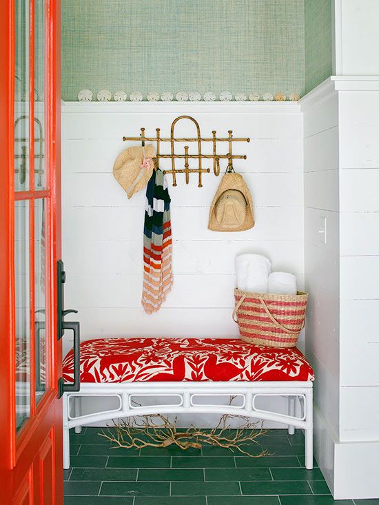 a pretty entryway with green grasscloth and a green tile floor, a coquelicot and white bench, a bamboo rack and a coquelicot door