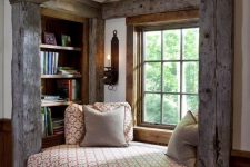 a pretty reading nook with rough and aged wood beams, built-in shelves, a daybed with chairs and additional book storage underneath
