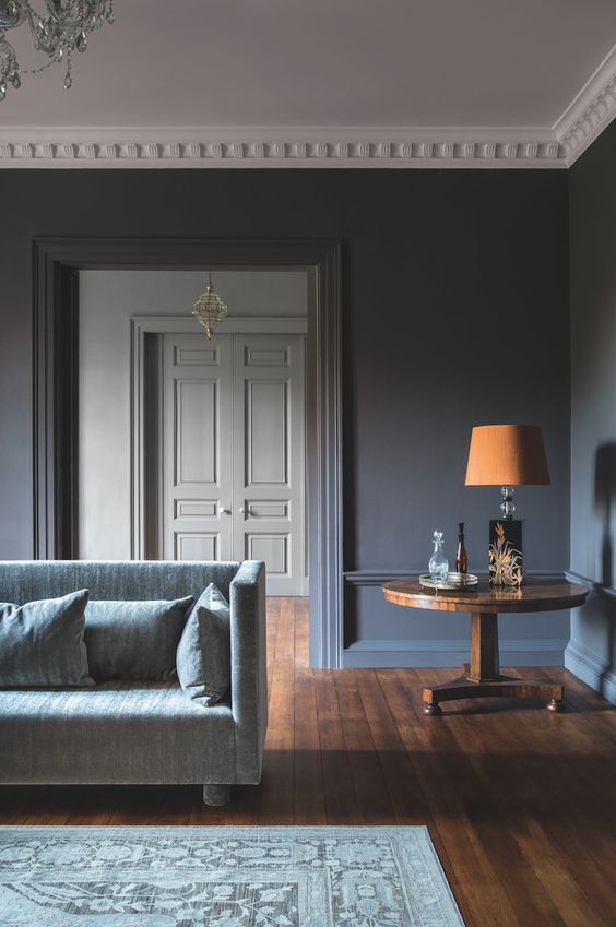 a refined slate grey living room with a grey sofa, a wooden side table with a bold orange lamp is a chic space