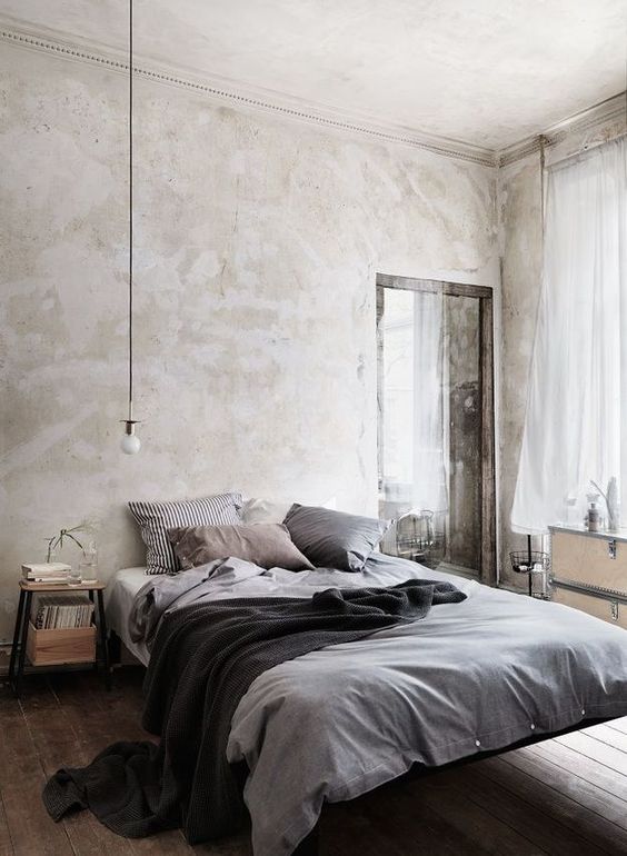 a relaxed bedrom with neutral limewashed walls, a floating bed, light stained furniture and grey bedding
