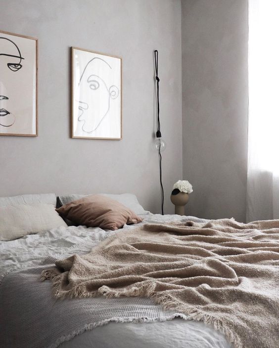 a relaxed bedroom-with grey limewashed walls a bed with neutral bedding a mini gallery wall and a bulb hanging