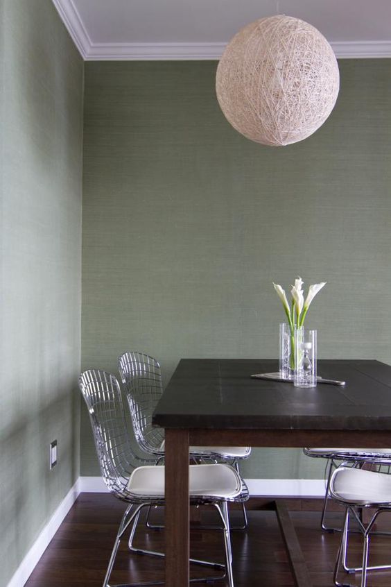 a simple dining space with green grasscloth wallpaper, a dark stained table, wire chairs and a yarn ball lamp