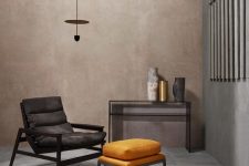 a stylish nook with a taupe limewashed wall, a black chair with a yellow footrest, a glass console table and a pendant lamp