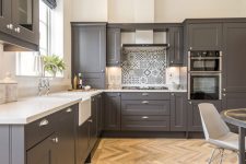 a stylish slate grey kitchen with shaker style cabinets, white countertops, a printed tile backsplash and built-in lights