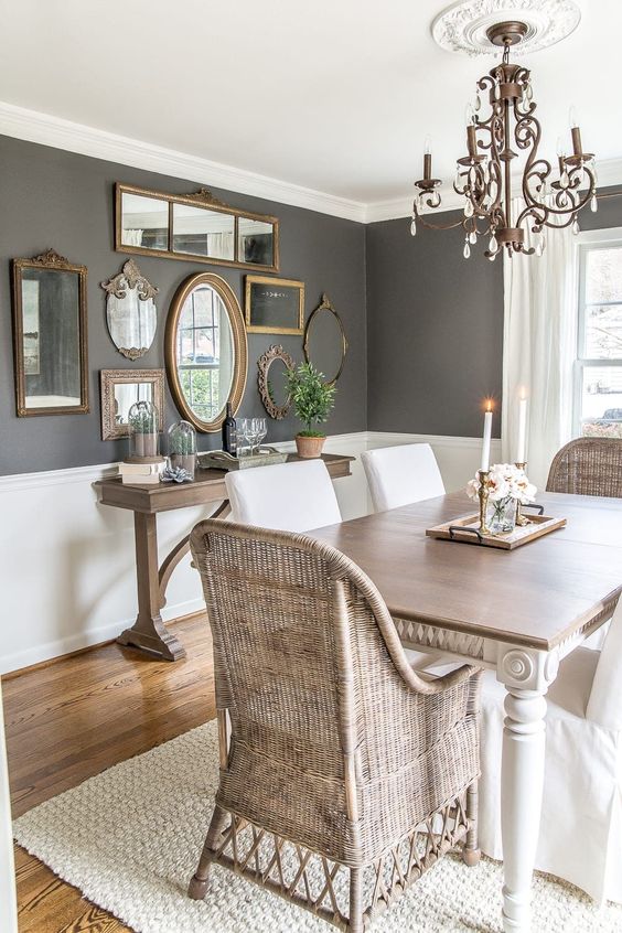 a stylish vintage dining room with slate grey walls with white wainscoting, a vintage dining table and woven chairs, a wooden console table