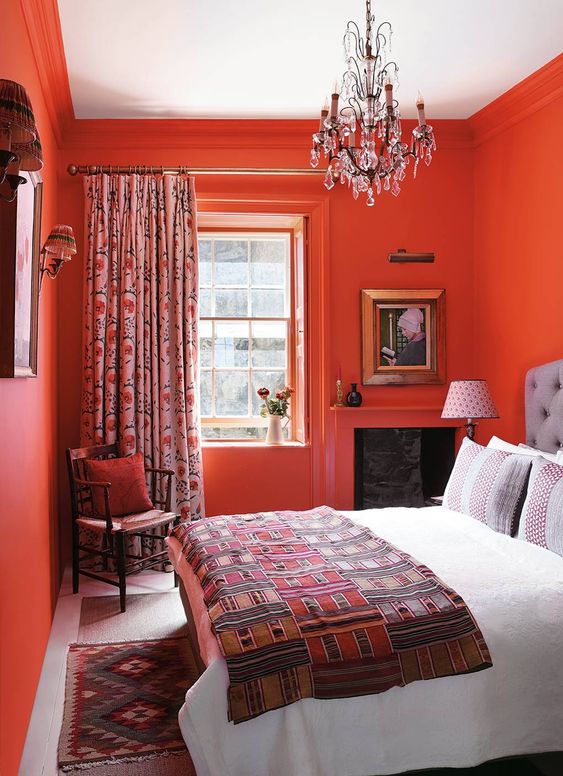 a super bold coquelicot bedroom with vintage stained furniture, printed bedding and curtains and wall sconces is amazingly energetic