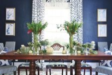 a vintage dining room with navy grasscloth wallpaper, a dark-stained dining table, striped chairs, a crystal chandelier and greenery