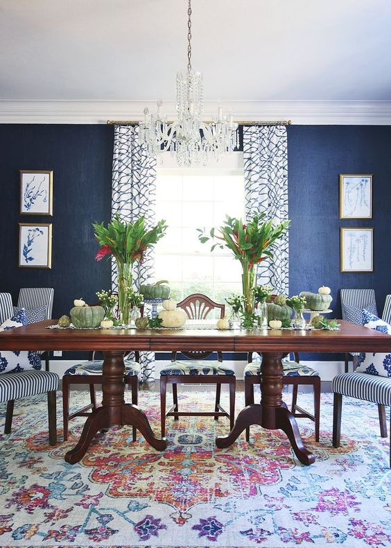 a vintage dining room with navy grasscloth wallpaper, a dark stained dining table, striped chairs, a crystal chandelier and greenery
