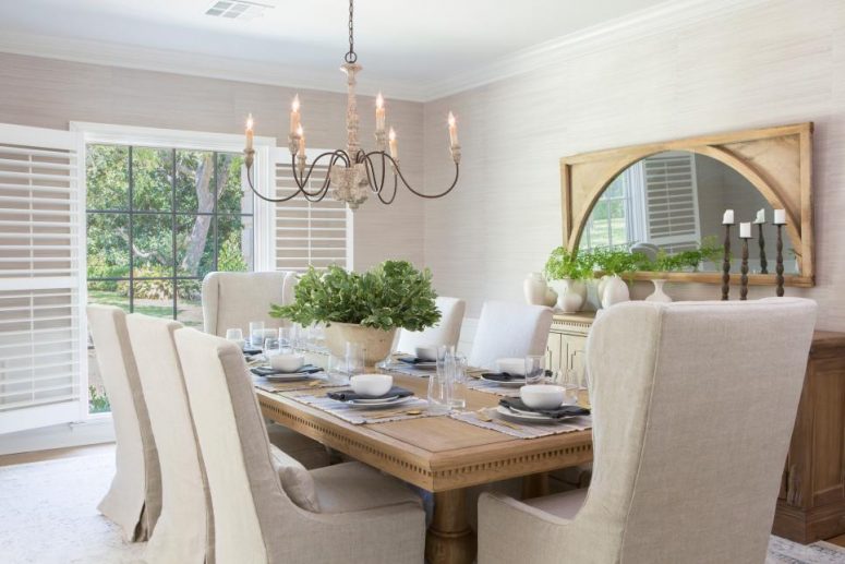 a vintage neutral dining room with light grey grasscloth wallpaper, a vintage wooden table and credenza, neutral upholstered chairs and a vintage chandelier