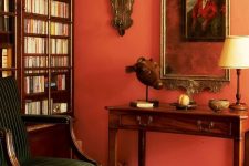 a vintage reading space with a coquelicot wall, heavy dark-stained furniture, a bookcase, a mirror and vintage artwork