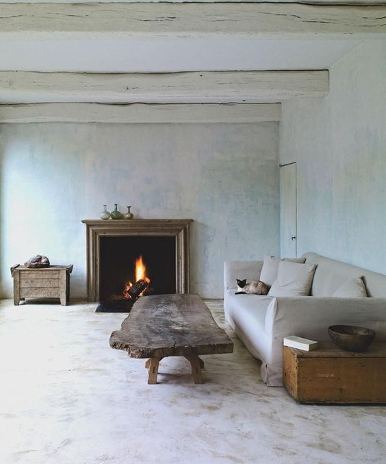 a wabi sabi living room with neutral limewashed walls, a fireplace, a neutral sofa, a rough wood coffee table and chests