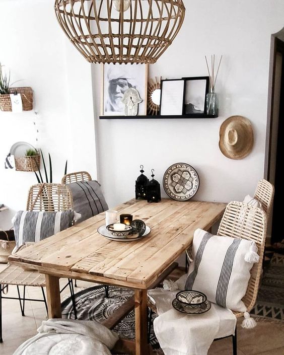 a welcoming Scandinavian dining space with a rough wood table, rattan chairs and a pendant lamp, beautiful plates and striped pillows