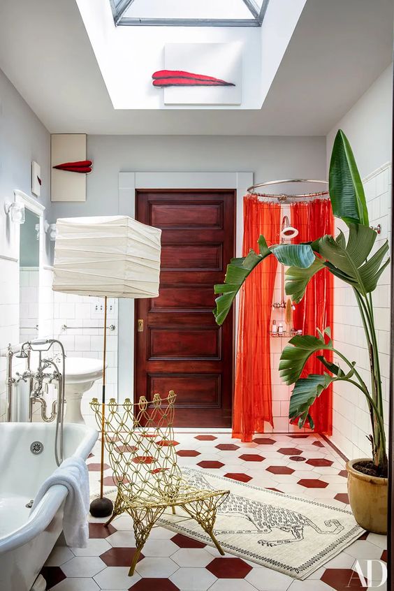 a whimsical bathroom with a hex tile floor, a clawfoot tub, a shower space with coquelicot curtains, a floor lamp and a gold chair