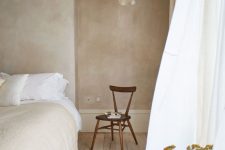 an airy bedroom with tan limewashed wall, a white bed with neutral bedding, a catchy pendant lamp and a chair