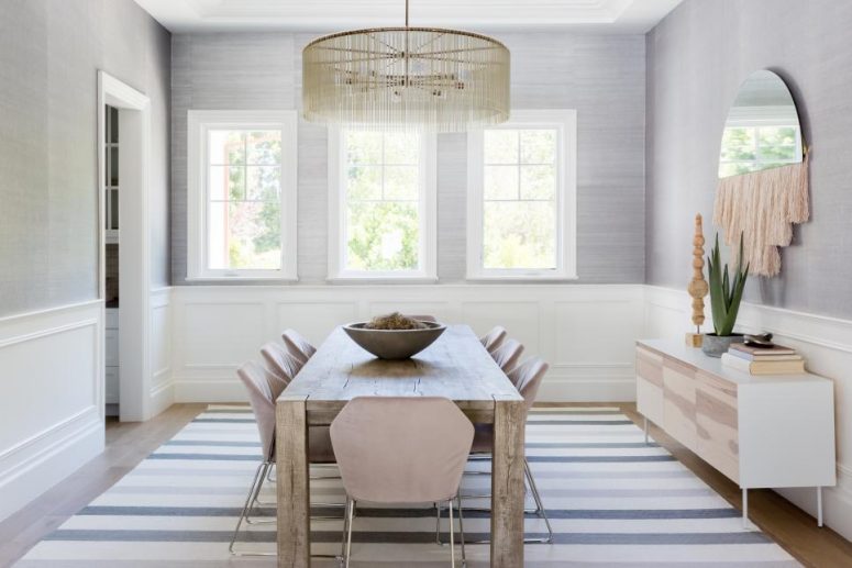 an airy dining room with grey grasscloth wallpaper and wainscoting, a reclaimed wood table, lilac chairs and a boho mirror