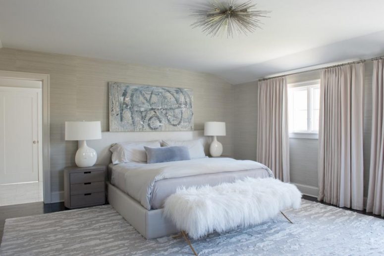 an airy neutral bedroom with light grey grasscloth wallpaper, a dove grey bed and grey nightstands, a printed rug and blush curtains