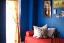 an electric blue space with a coquelicot daybed, printed pillows, a gallery wall and sconces