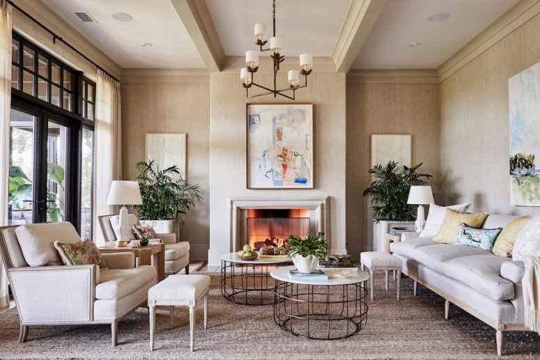 an elegant neutral living room done with tan grasscloth wallpaper, a stylish fireplace, neutral furniture, beautiful artworks and potted plants