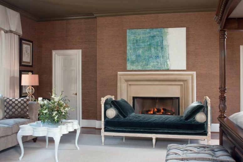 an elegant vintage living room with brown grasscloth wallpaper, a built-in fireplace with a chic mantel, a dark green daybed, a grey sofa, a vintage white table