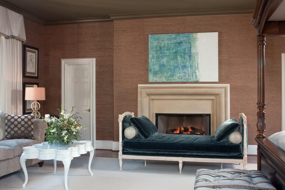 an elegant vintage living room with brown grasscloth wallpaper, a built in fireplace with a chic mantel, a dark green daybed, a grey sofa, a vintage white table