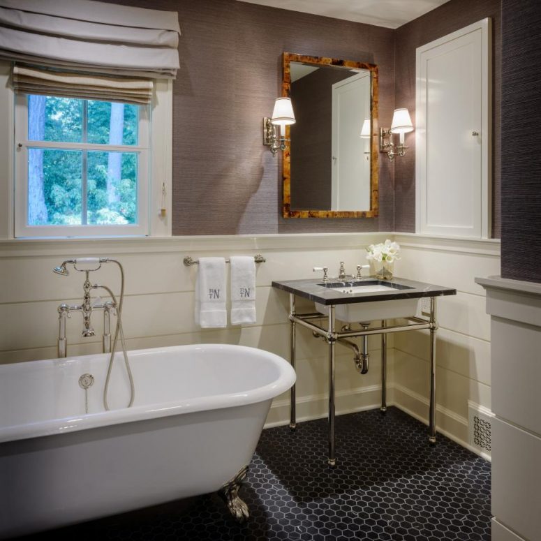 an exquisite vintage bathroom with taupe grasscloth wallpaper, white wainscoting, a clawfoot tub, a vintage free-standing sink and Roman shades